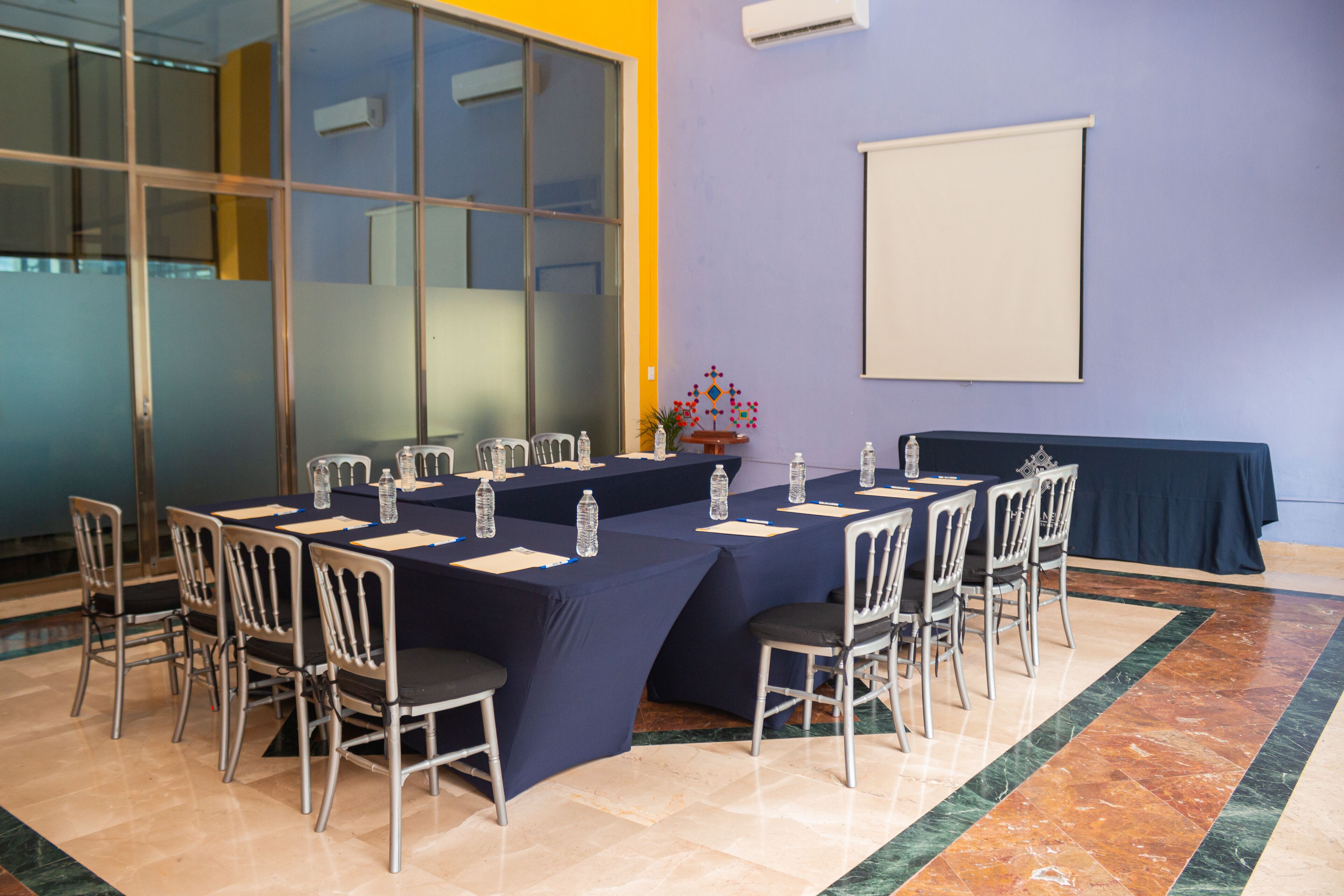 Una sala de conferencias con una gran mesa, sillas y una pantalla para proyector.