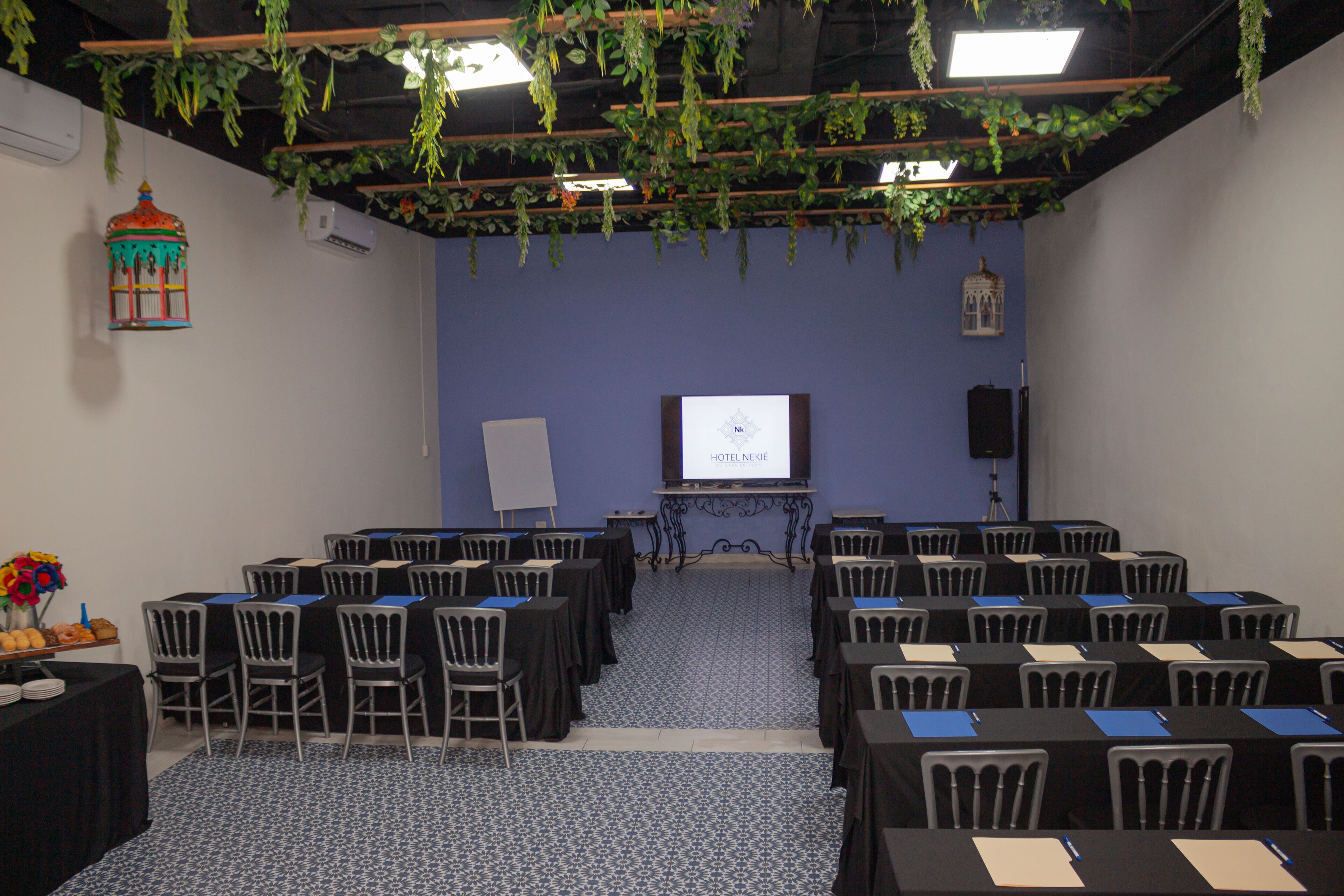Ein Konferenzraum mit Tischen und Stühlen, die für eine Besprechung bereitstehen, einer Projektionsleinwand und einer Pflanze, die von der Decke hängt.