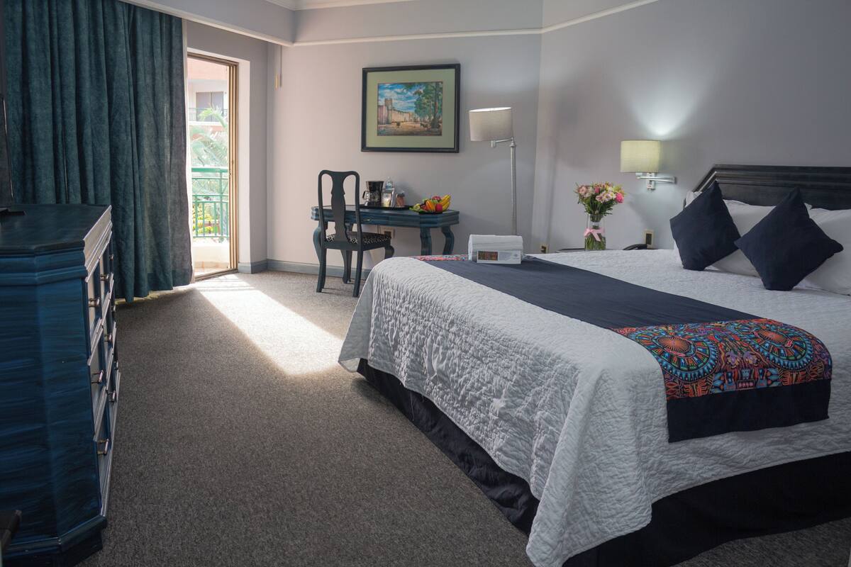 A hotel room with a large bed, a desk with a chair, a lamp, and a painting on the wall.