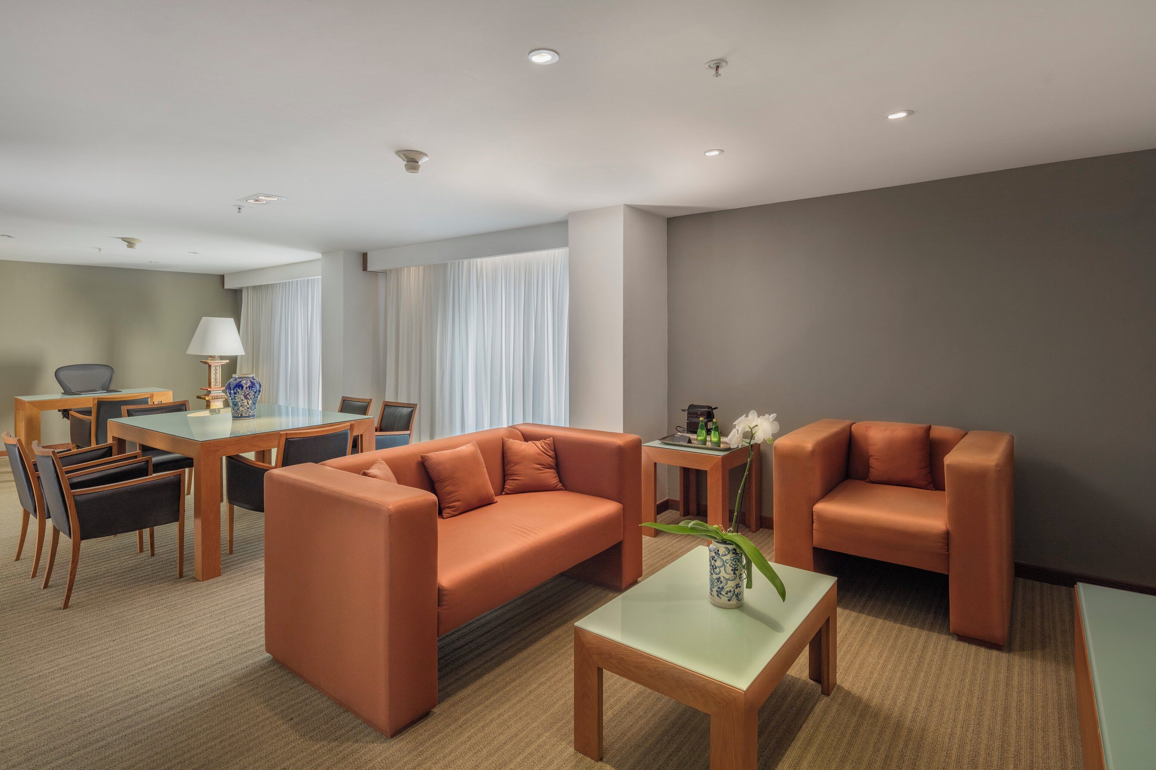 A modern hotel room with a sofa, armchair, dining table, and chairs.