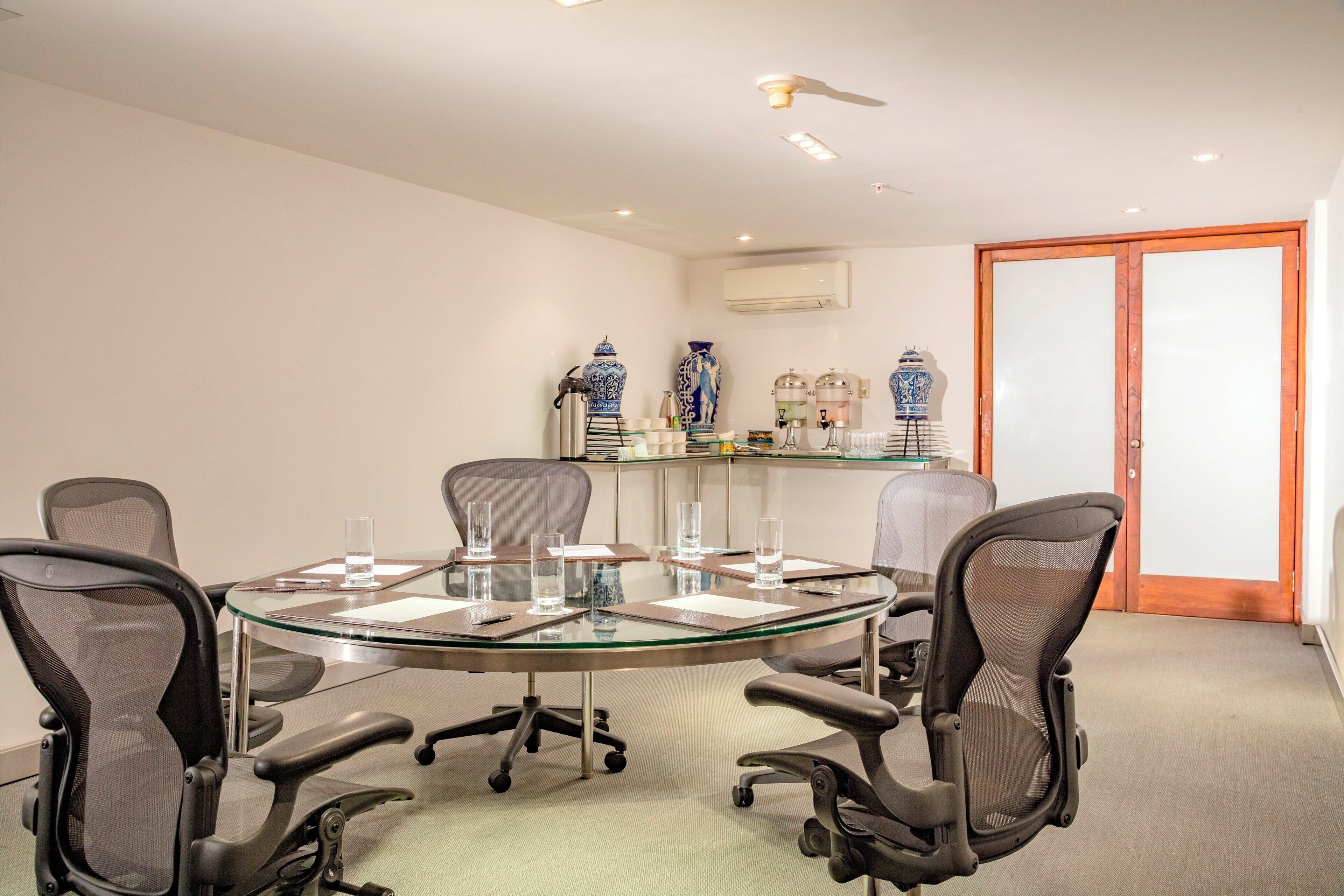 Une salle de conférence avec une table en verre, quatre chaises de bureau et des vases décoratifs disposés sur une étagère.