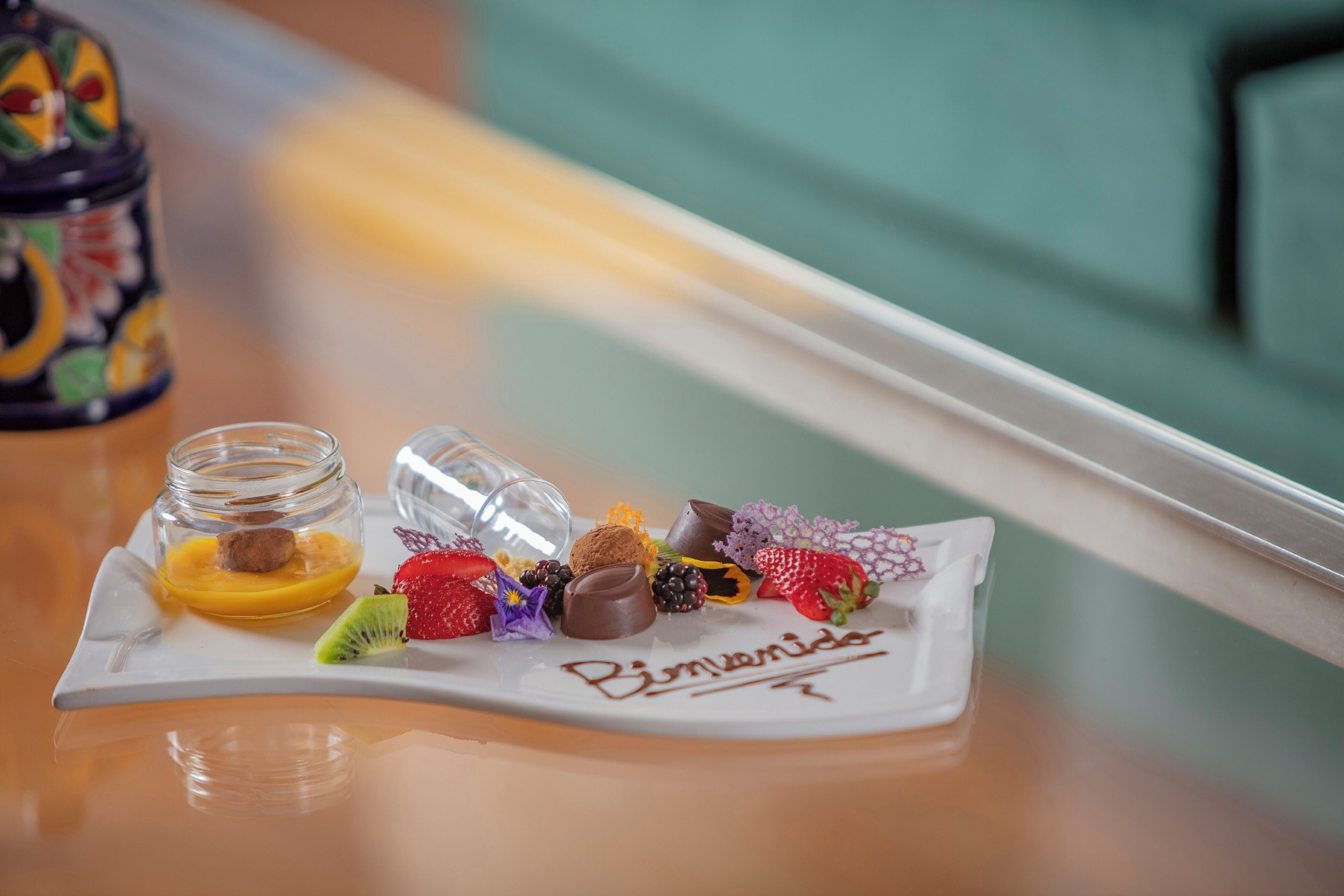 Une assiette de desserts, avec divers bonbons et fruits, est posée sur une table près d’une fenêtre.