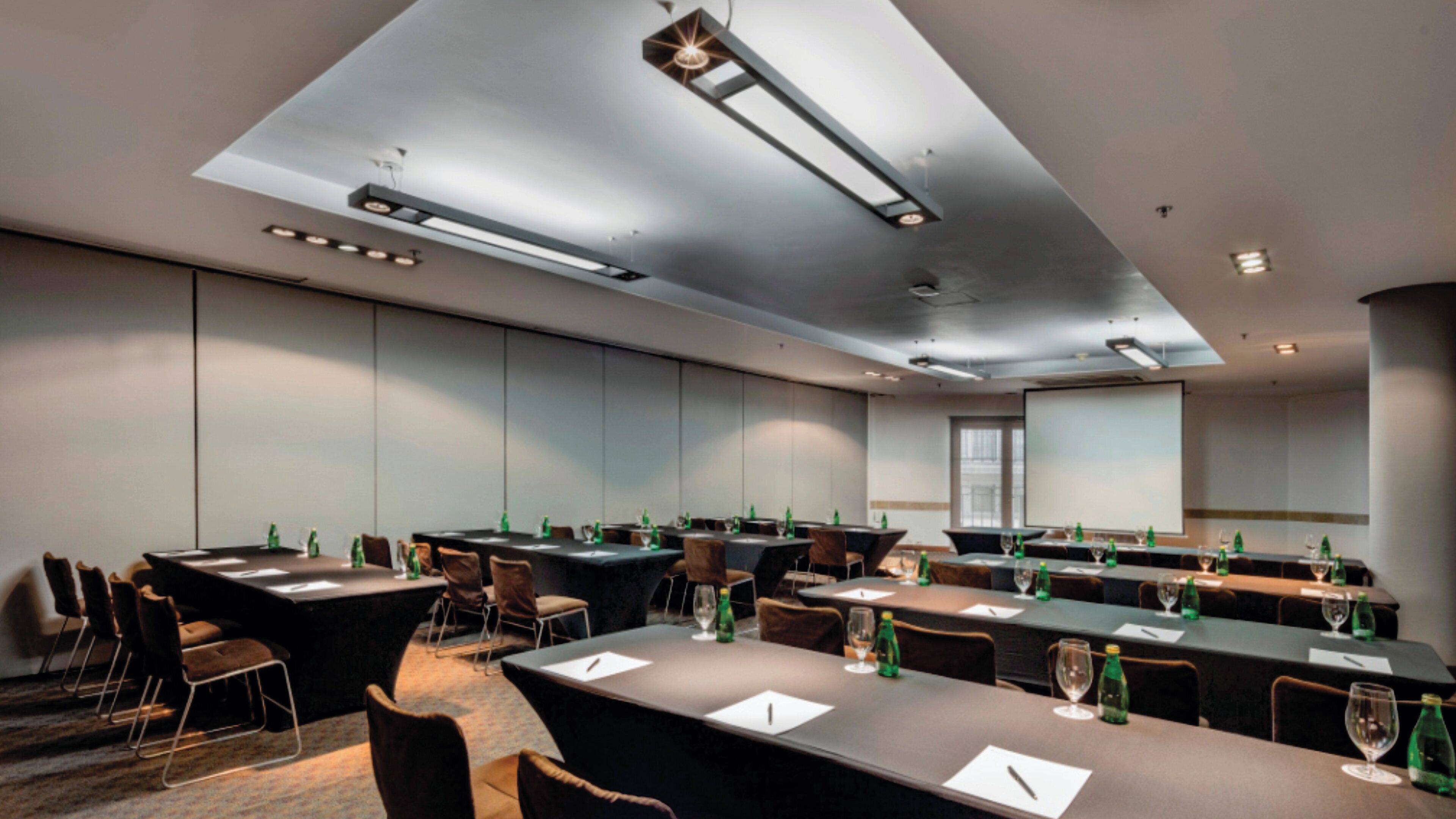 A conference room with multiple tables, chairs, and a projector screen.
