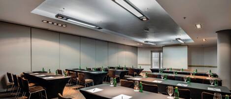 Un salón de conferencias con varias mesas, sillas y una pantalla para proyector.