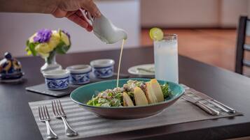 A table with a bowl of salad, a glass of iced tea, and a hand pouring dressing.