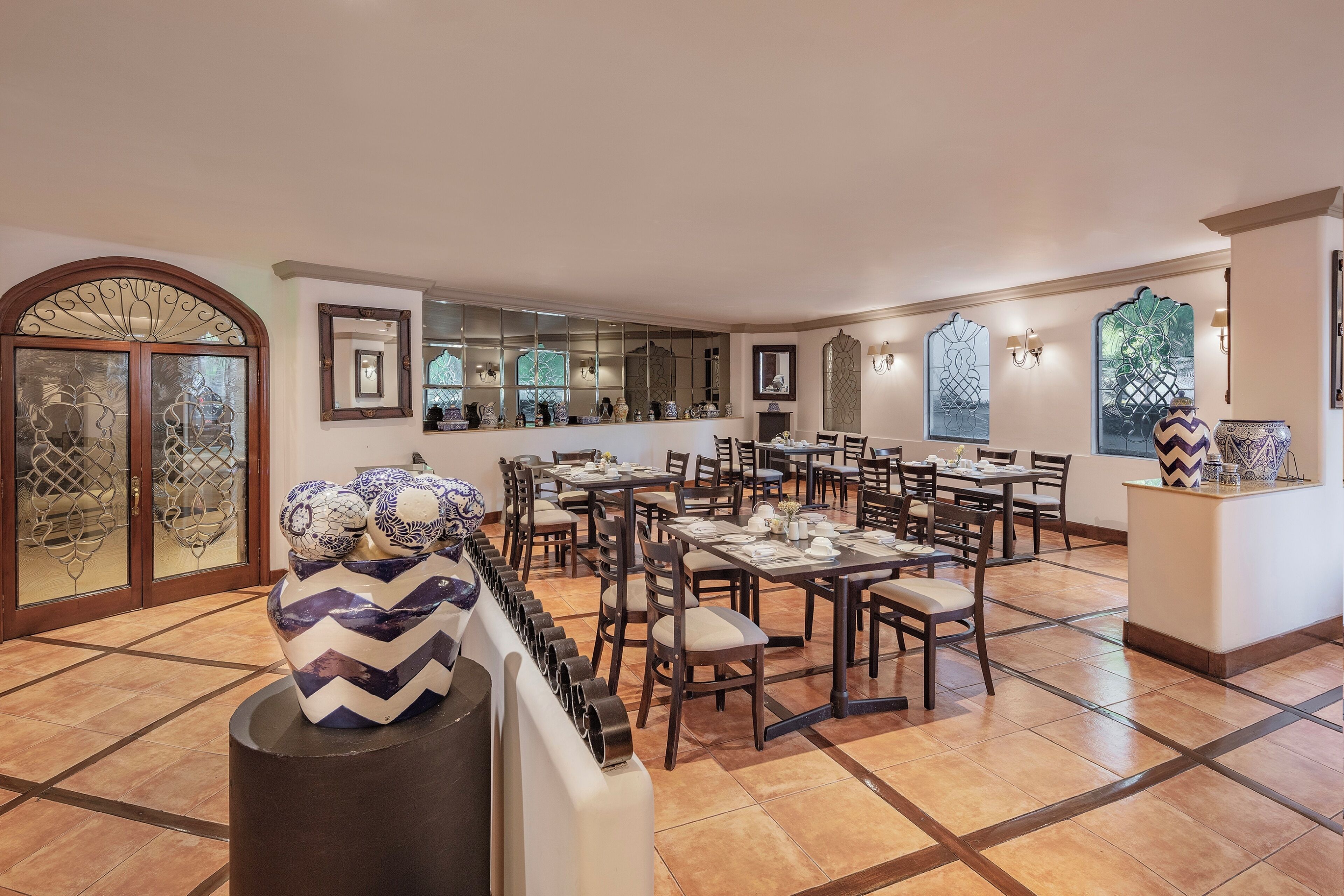 A spacious dining area with multiple tables and chairs, a decorative vase, and a mirror reflecting the room.