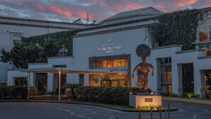 A building with a statue in front, a sign reading "Presidencia Intercontinental FESCA", and a well-maintained garden area. - InterContinental Presidente Puebla by IHG (Puebla)