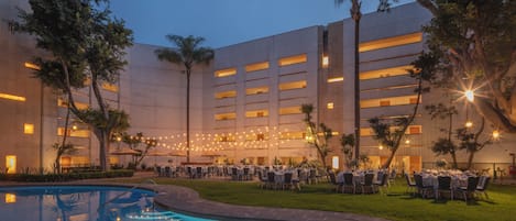 A hotel courtyard with a swimming pool, outdoor seating, and string lights.