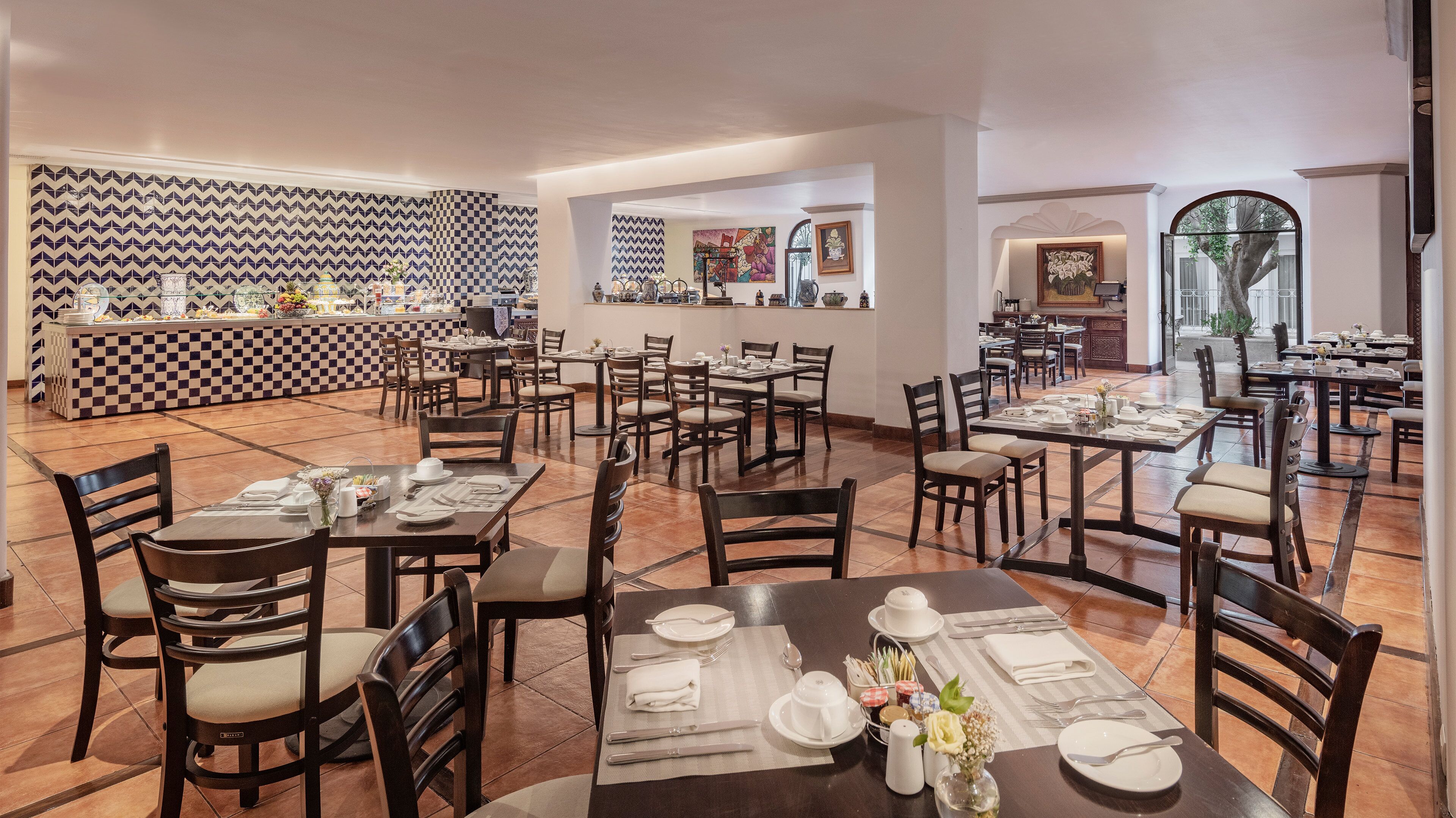 A spacious dining area with multiple tables and chairs, a buffet counter, and a view of the outdoors through large windows.