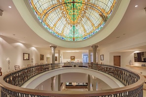 Un amplio vestíbulo de hotel con una cúpula central de vitrales, una escalera curva y un mostrador de recepción.