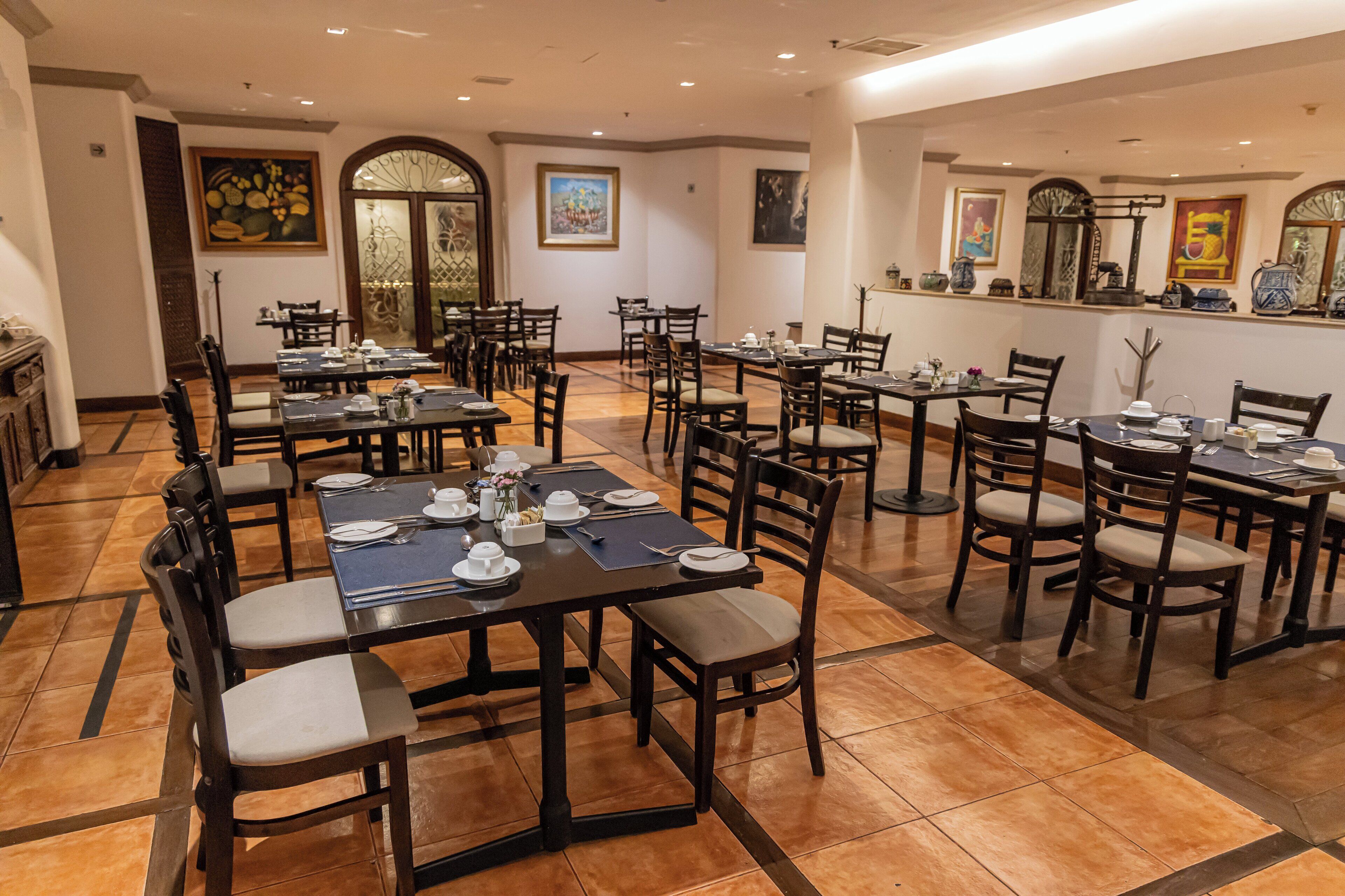 A spacious dining area with multiple tables and chairs, featuring a tiled floor and artwork on the walls.