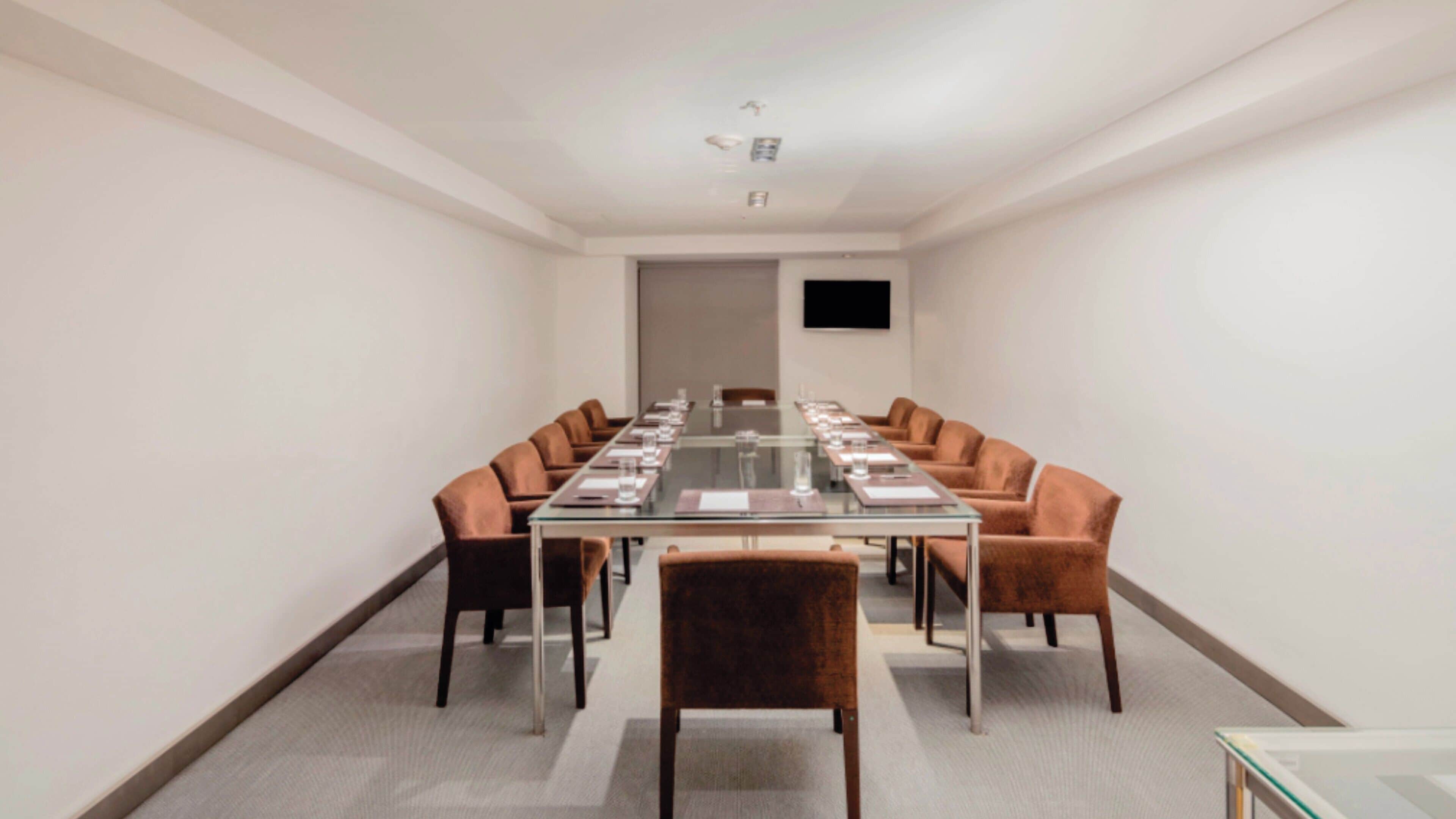 Un salón de conferencias con una larga mesa, sillas y un televisor de pantalla plana en la pared.