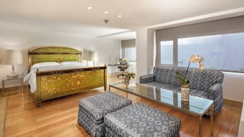 A hotel room with a bed, a sofa, a glass coffee table, and a view of the sky.