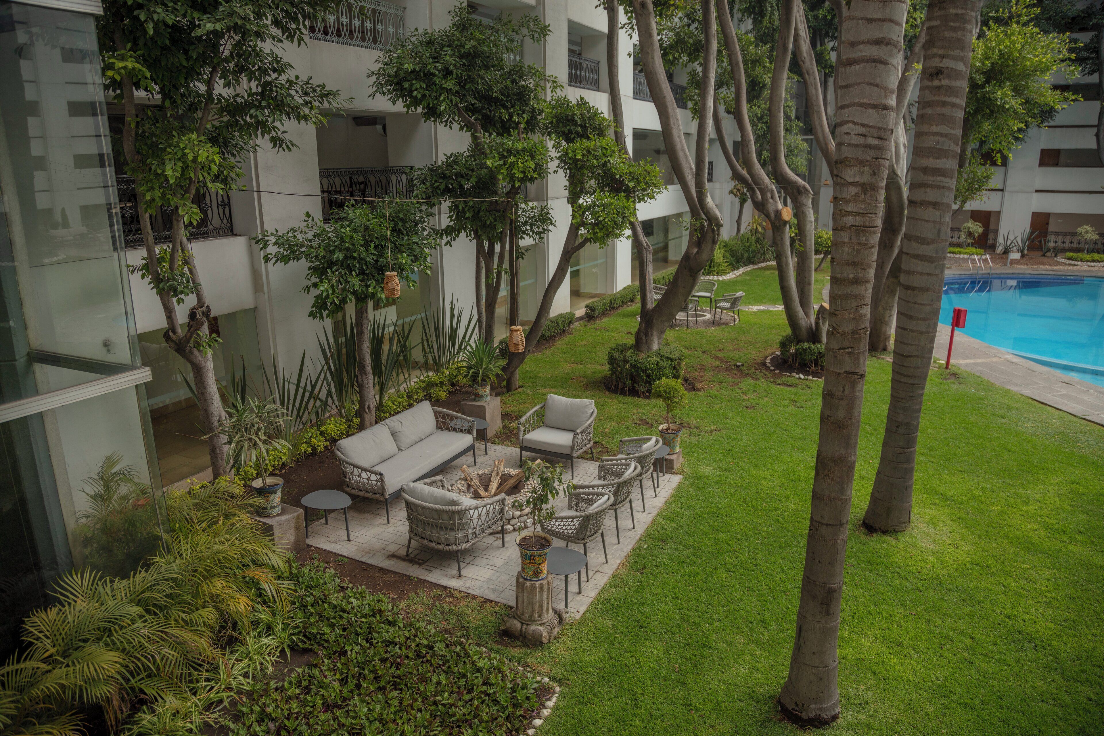 Un patio con mobiliario exterior, piscina y abundante vegetación.