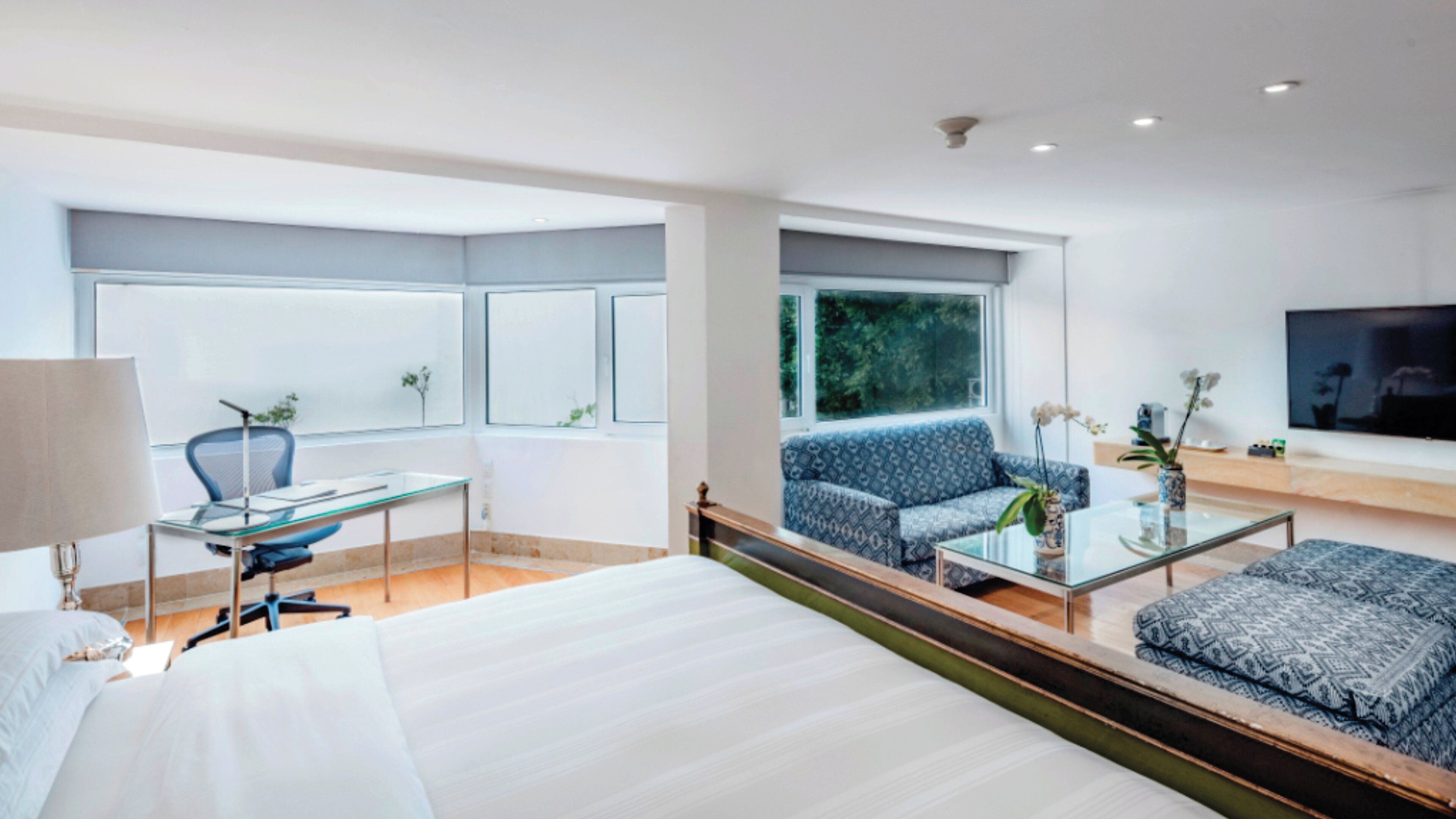 A modern hotel room with a large bed, a desk, a sofa, and a TV.
