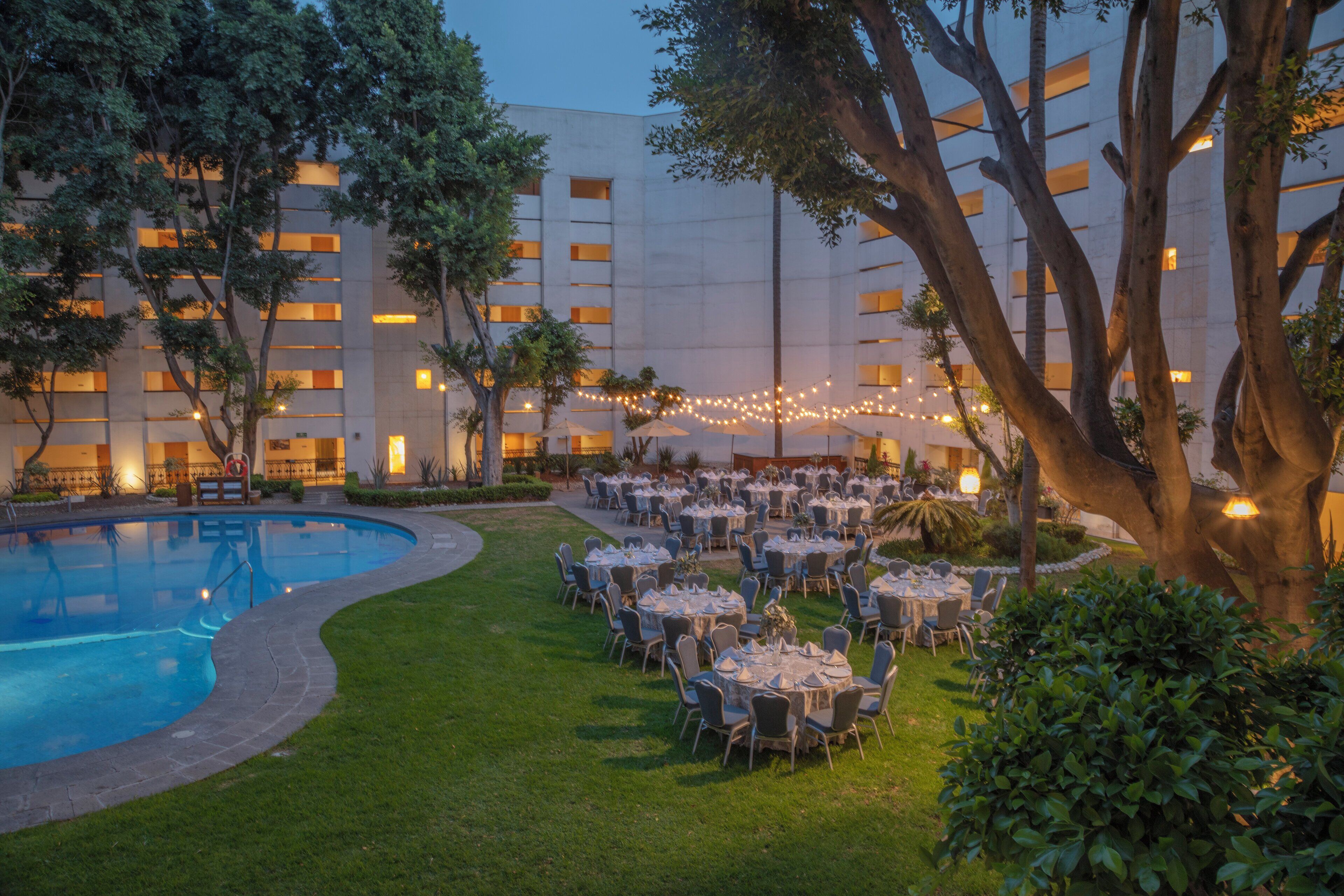A hotel courtyard with a swimming pool, outdoor seating, and string lights.