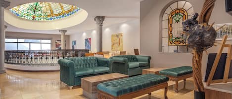 A spacious lobby with green upholstered sofas, a wooden bench, and a large stained glass window.