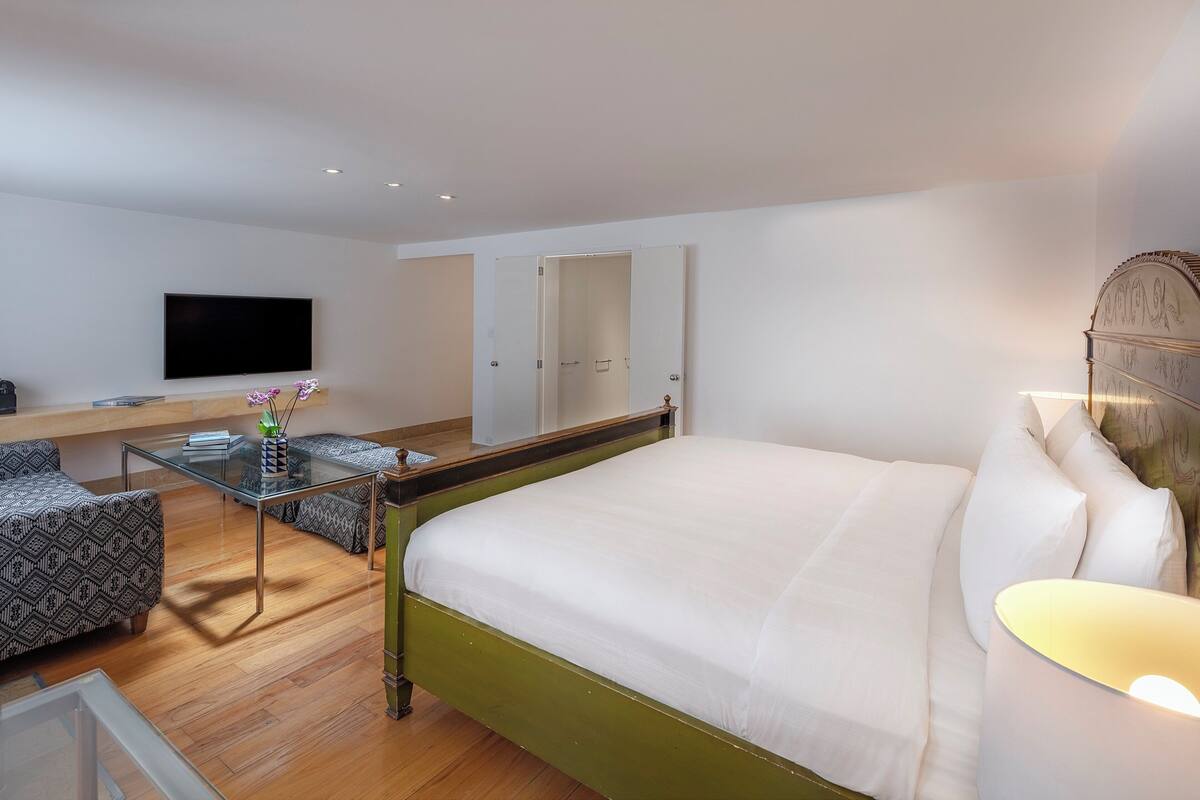 Una habitación de hotel moderna con una cama verde, una mesa de centro de vidrio, un televisor de pantalla plana y un espejo grande.
