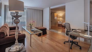 Quarto de hotel moderno com sofá marrom, mesa de centro de vidro, escrivaninha com cadeira e abajur.