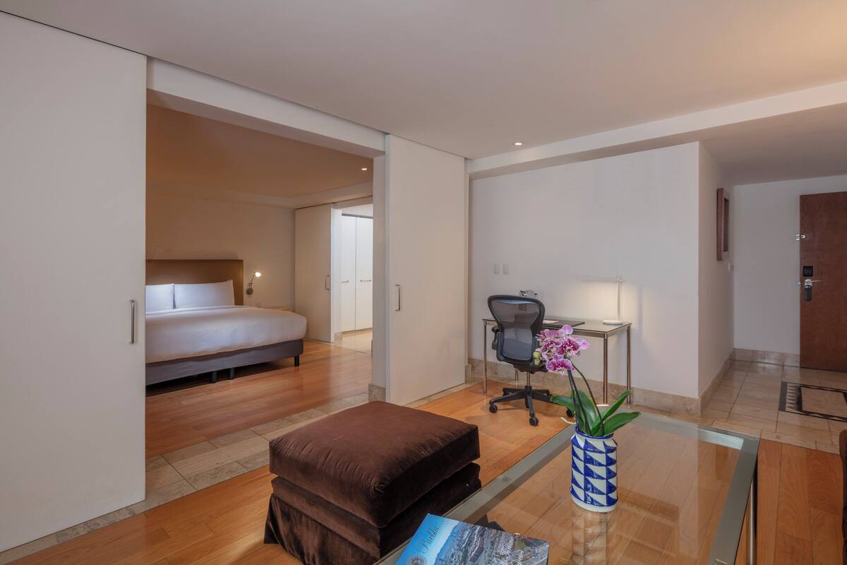 Una habitación de hotel moderna con una cama, un escritorio, una silla y una pequeña mesa con un jarrón de flores.