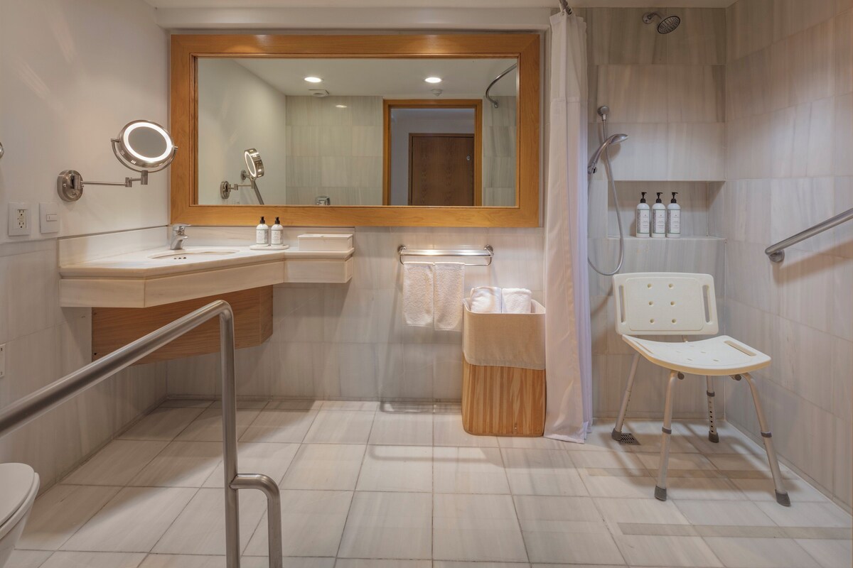 Un baño moderno con un espejo grande, un lavabo, un inodoro, una ducha y una barra de apoyo.