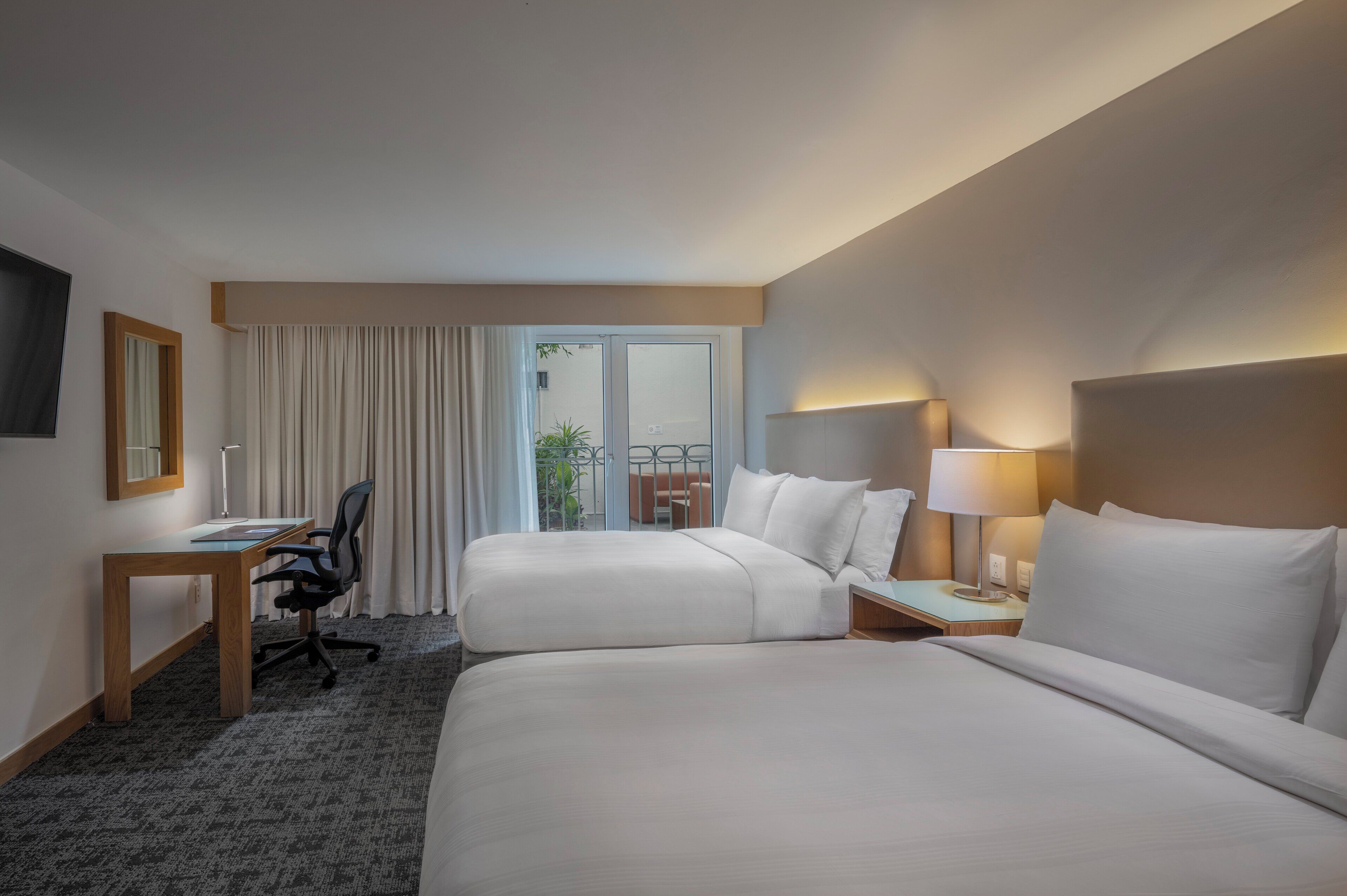 A hotel room with two beds, a desk, a chair, and a TV on the wall.