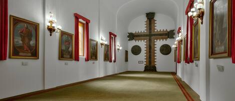 A corridor with framed religious paintings, a large cross, and red curtains.