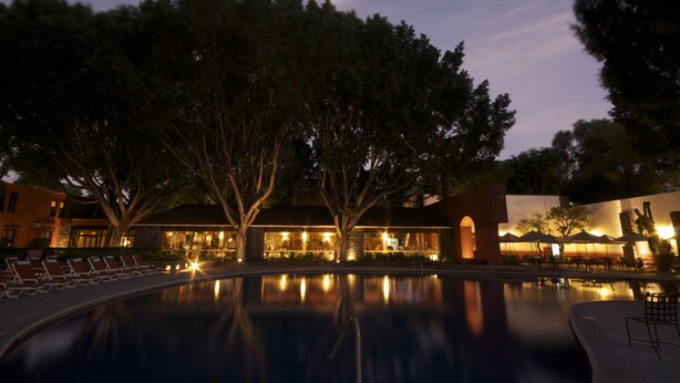 A poolside area with lounge chairs and a building with illuminated windows at dusk. - Hacienda Jurica by Brisas (Querétaro)