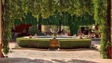 Un jardín con una fuente central, rodeado de setos y árboles bien cuidados.
