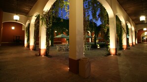 An outdoor courtyard with arches, tables, and chairs, illuminated by ambient lighting. - Hacienda Jurica by Brisas (Querétaro)