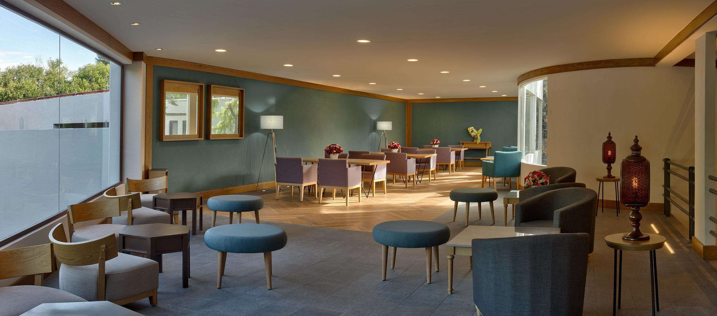 Un moderno vestíbulo de hotel con un área de descanso, una recepción y un ventanal con vistas a zonas verdes.