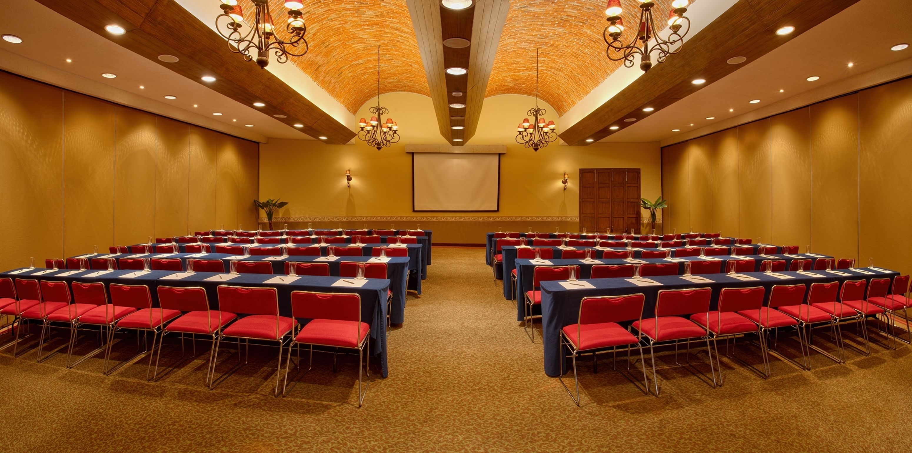Un salón de conferencias con filas de sillas rojas y mesas azules, equipado con micrófonos y tarjetas de identificación.