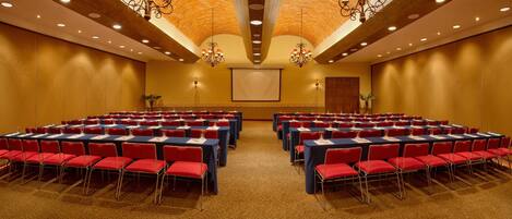 Un salón de conferencias con filas de sillas rojas y mesas azules, equipado con micrófonos y tarjetas de identificación.