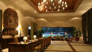 A spacious lobby with a reception desk, chairs, a large painting, and a view of a pool. - Hacienda Jurica by Brisas (Querétaro)