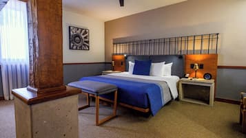 A hotel room with a large bed, a wooden bench, a ceiling fan, and a wall-mounted artwork.