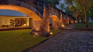 A historic stone bridge with a modern building on one side, featuring an open patio area. - Hacienda Jurica by Brisas (Querétaro)