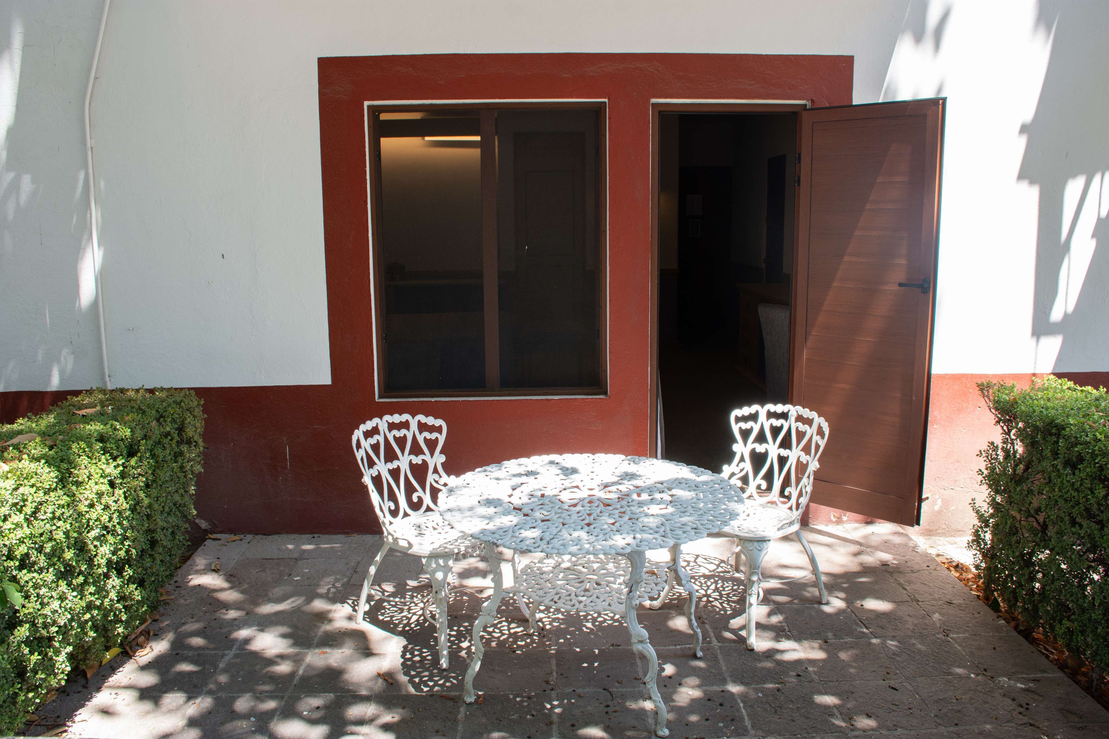 A patio with a round table and two chairs, a red and white wall, and a door.