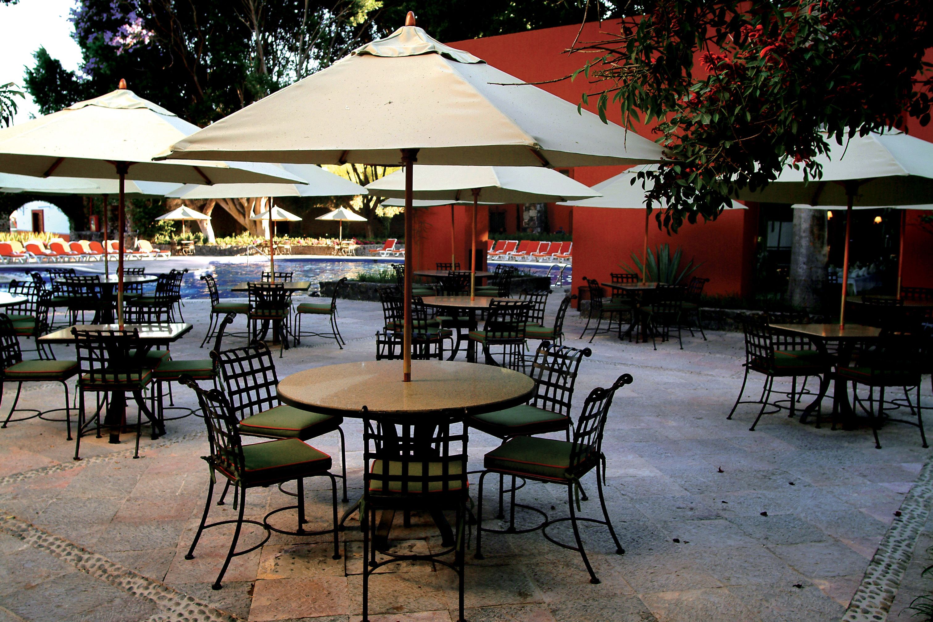 An outdoor patio area with round tables and chairs, surrounded by umbrellas.