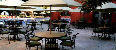 An outdoor patio area with round tables and chairs, surrounded by umbrellas.