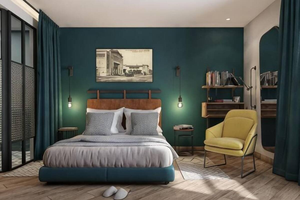 Een slaapkamer met een bed, een stoel, een boekenkast en een schilderij aan de muur.