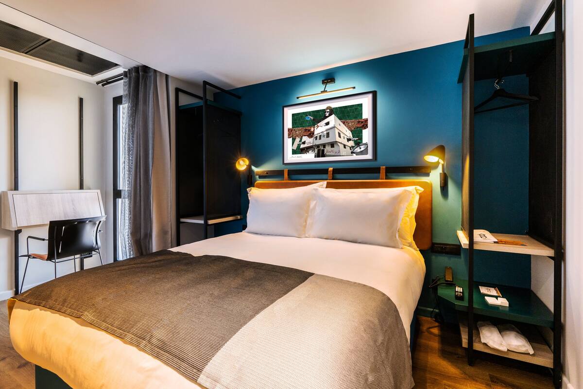 Een net opgemaakt bed met witte lakens, een nachtkastje met een lamp, en een lijst met een foto aan de muur.