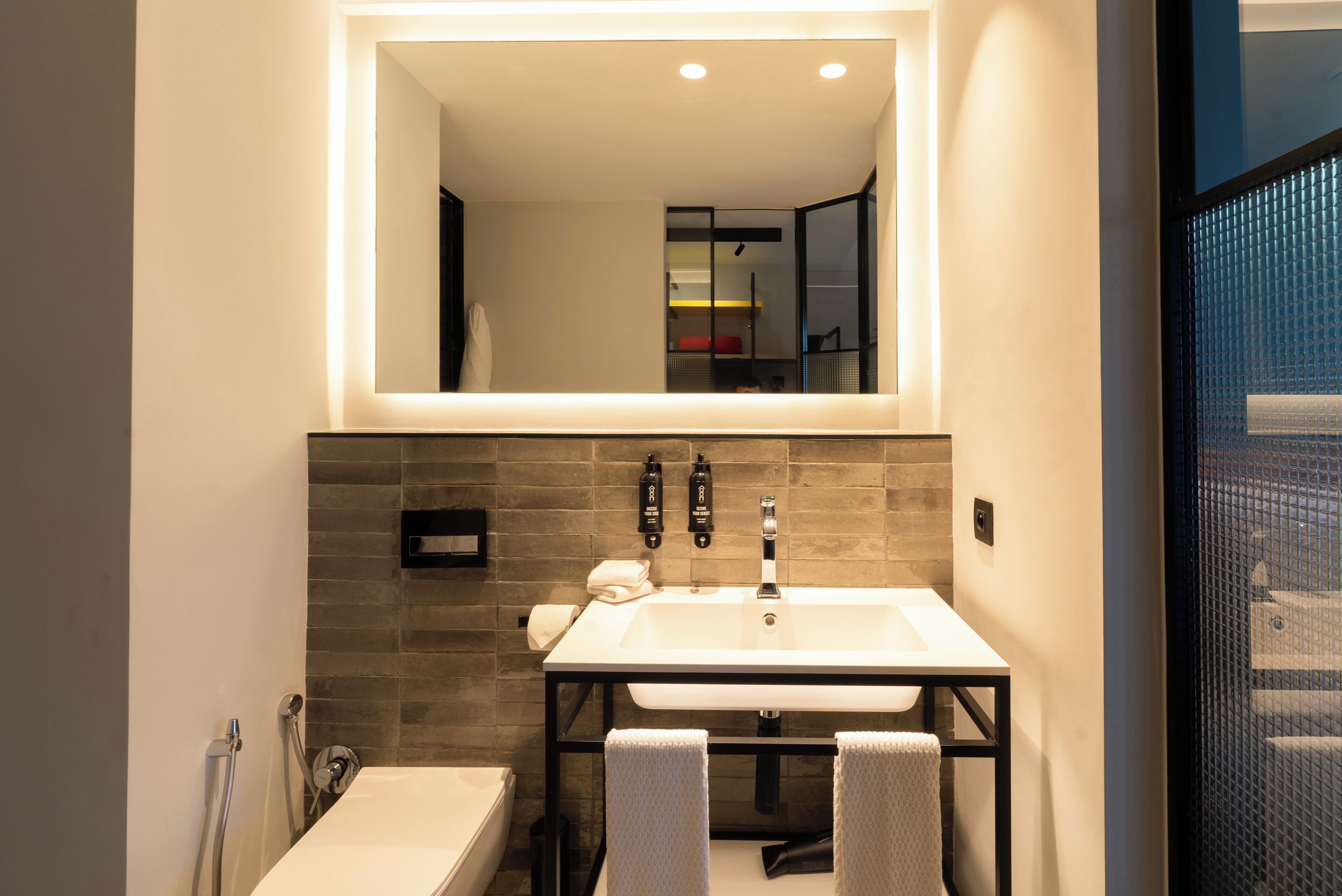 A modern bathroom with a large mirror, a white sink, and two towels hanging on hooks.