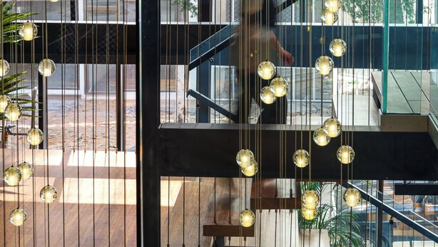 Un intérieur moderne avec un escalier à plusieurs niveaux, de grandes fenêtres et des luminaires sphériques suspendus.