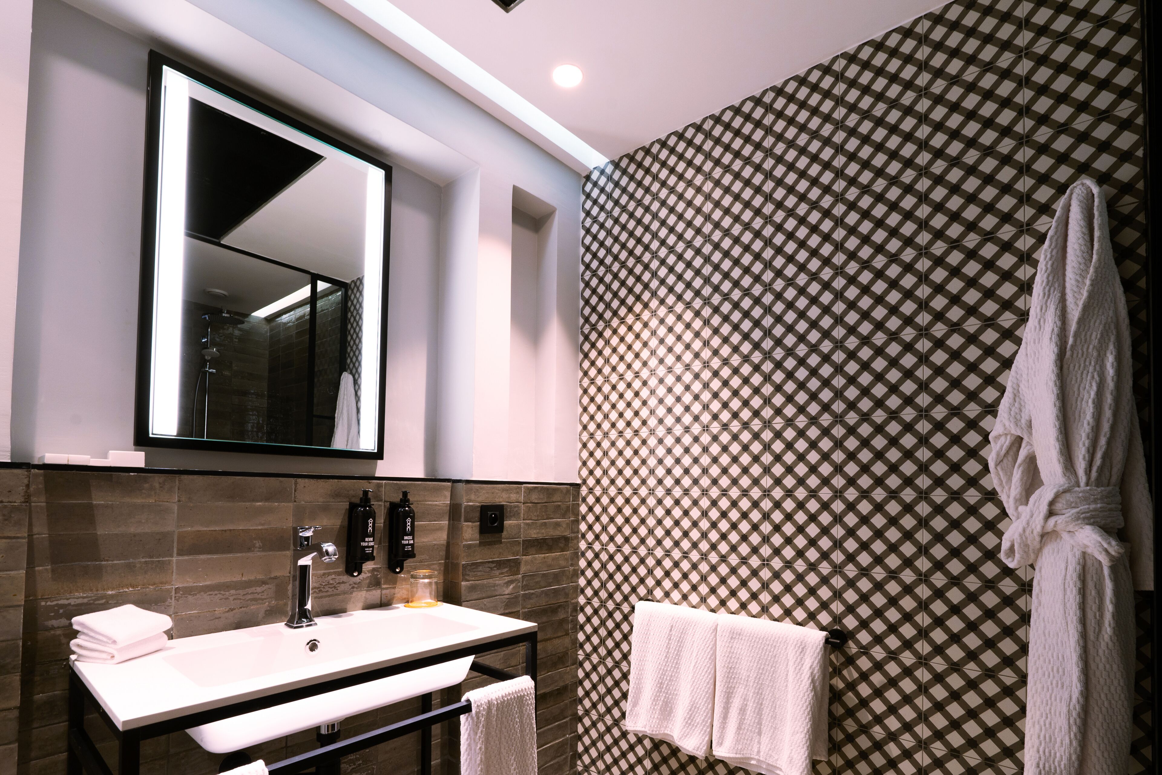 A modern bathroom with a large mirror, a white sink, and a patterned wall.