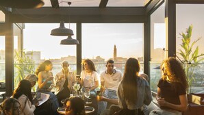 Un groupe de personnes est réuni autour d’une table dans un restaurant moderne, doté de grandes fenêtres et d’un éclairage suspendu.