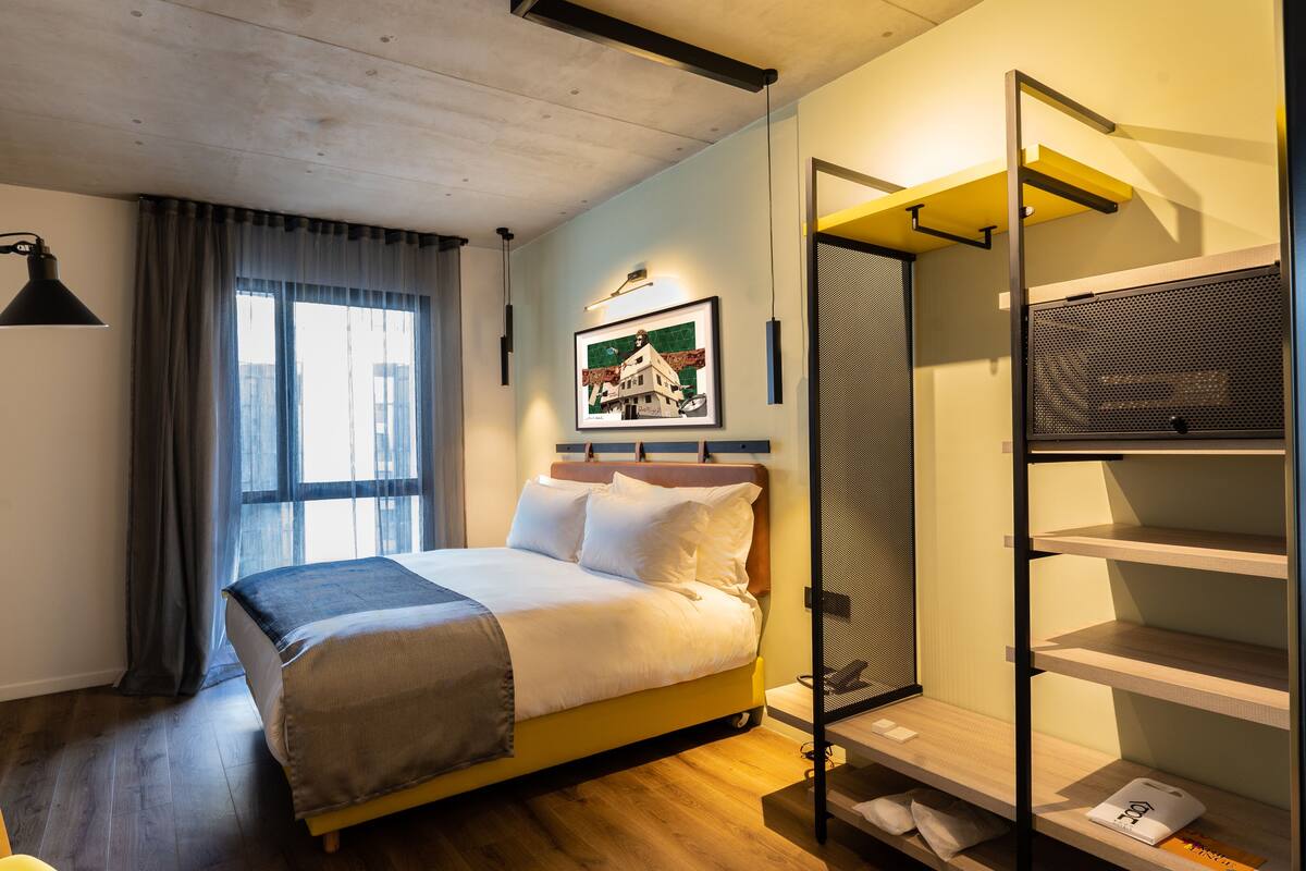 Een moderne hotelkamer met een bed, een bureau, een stoel, een kledingkast en een raam met gordijnen.