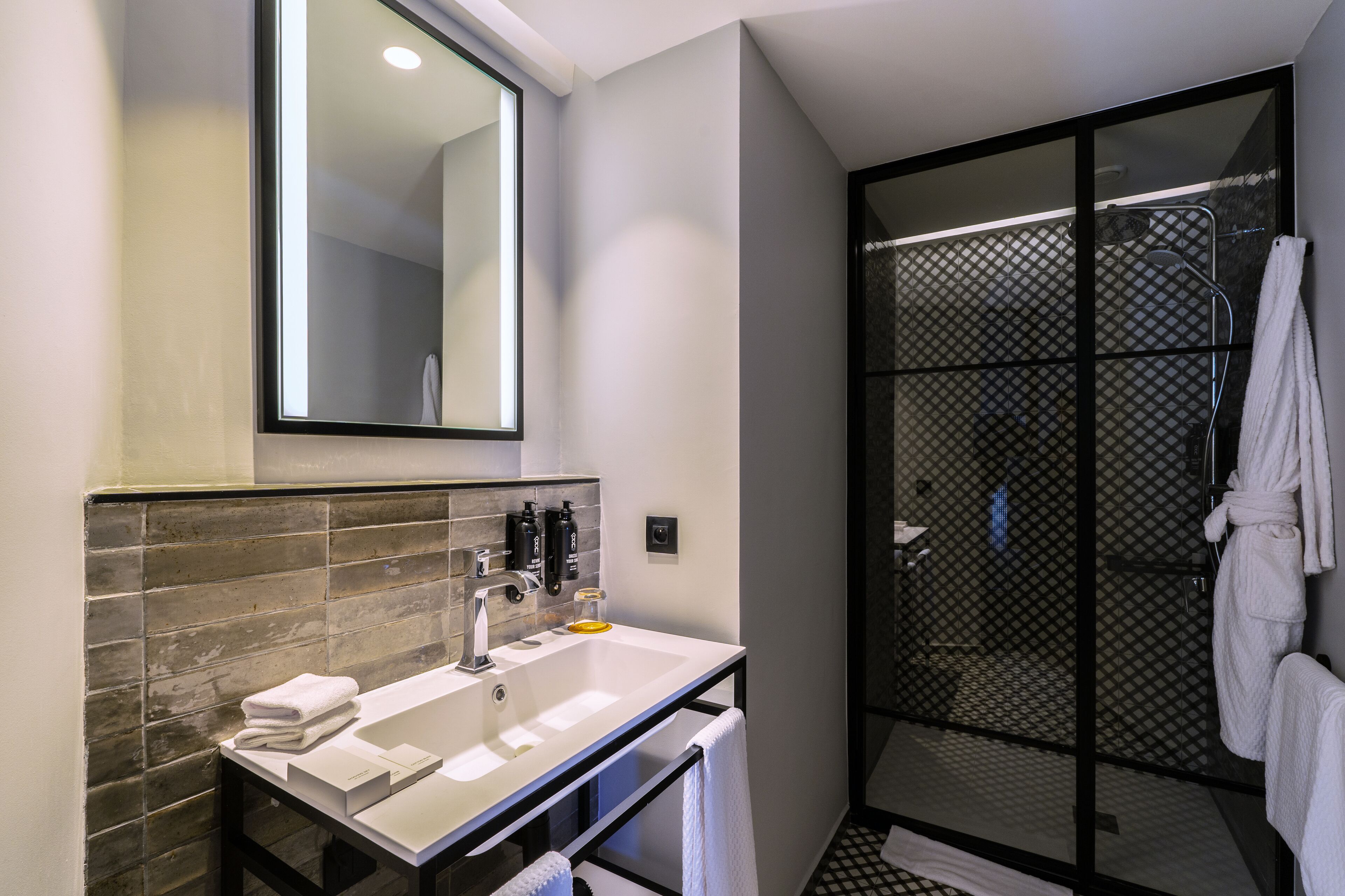 Un baño moderno con un espejo grande, un lavabo blanco y una zona de ducha con mampara de vidrio.