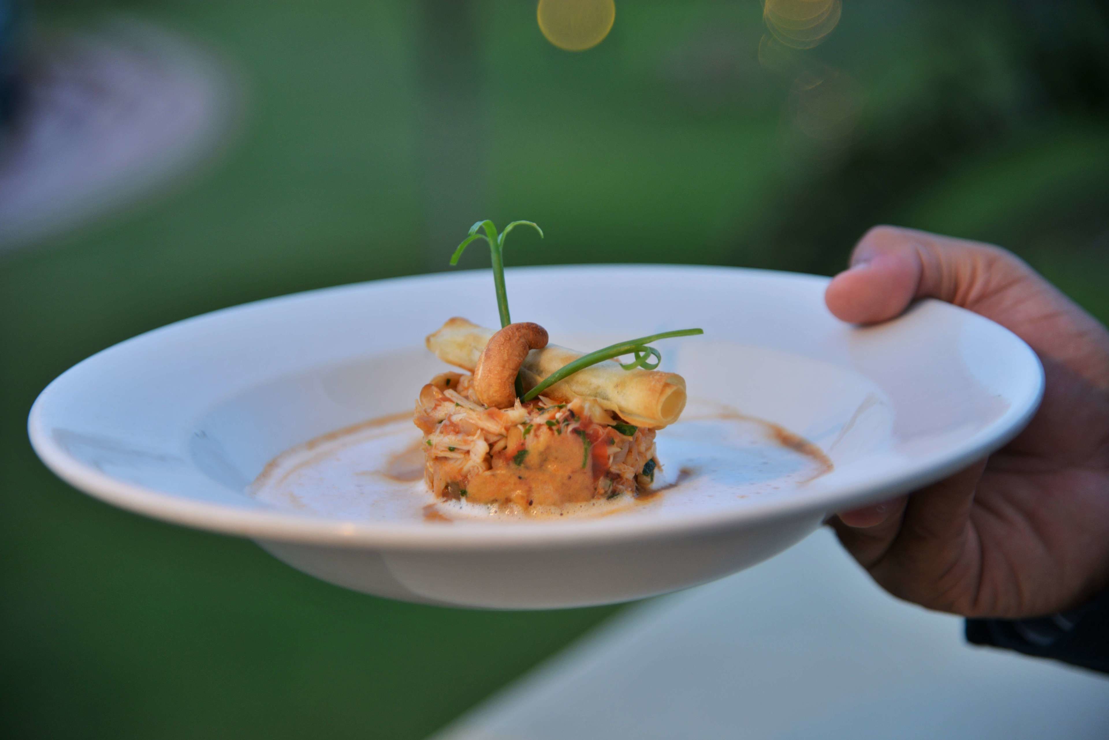 A white plate with a food dish, held by a hand.