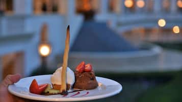 A dessert plate with a chocolate cake, strawberries, and a chocolate sauce, held in front of a building with lights in the background.