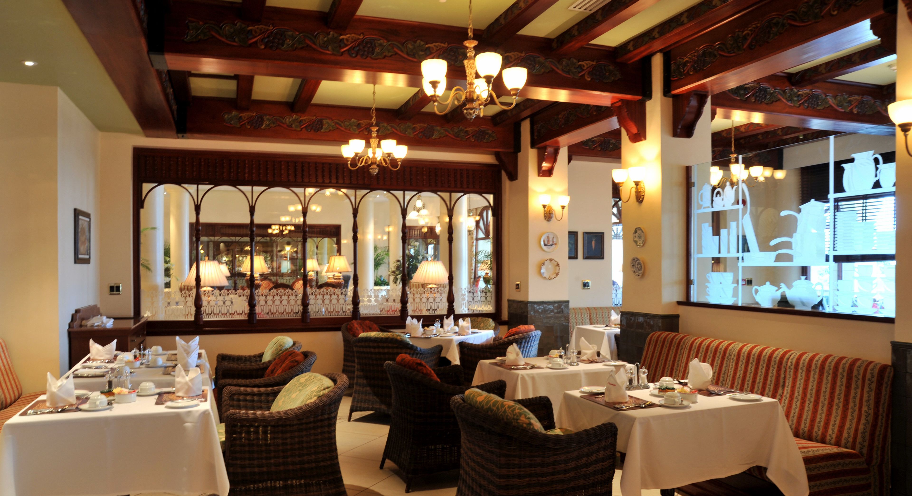A dining area with tables set for service, wicker chairs, and a large window with decorative items.
